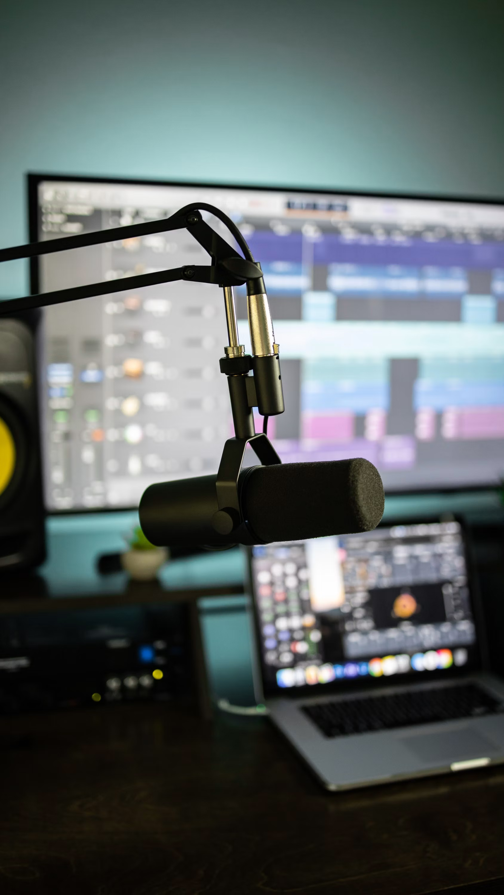 Shure SM7B microphone on a boom arm, with Logic Pro and a MacBook Pro in the background